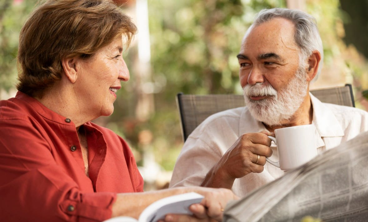 Two older adults talking together over a newspaper