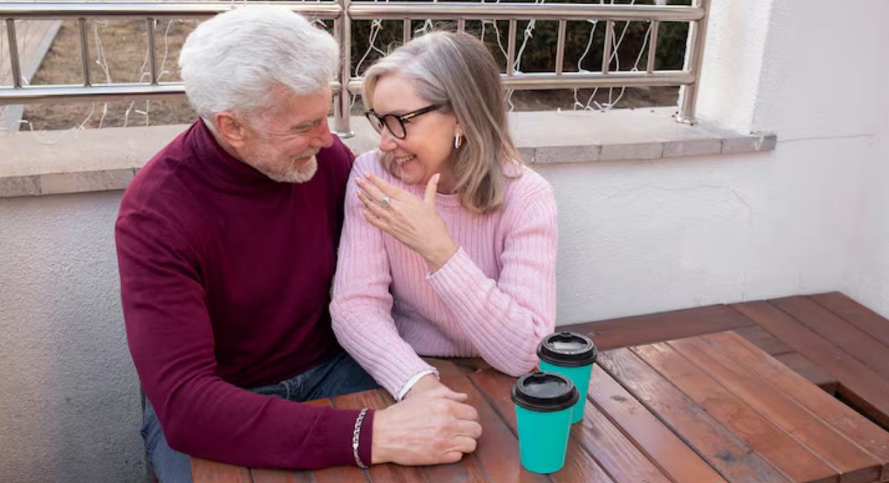 Two older adults sitting together with takeaway coffee